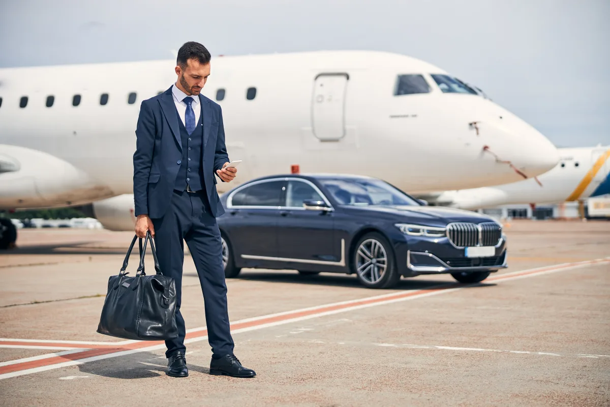 Business traveller booking an Excel Taxi Yeovil airport transfer by phone beside a car near the terminal